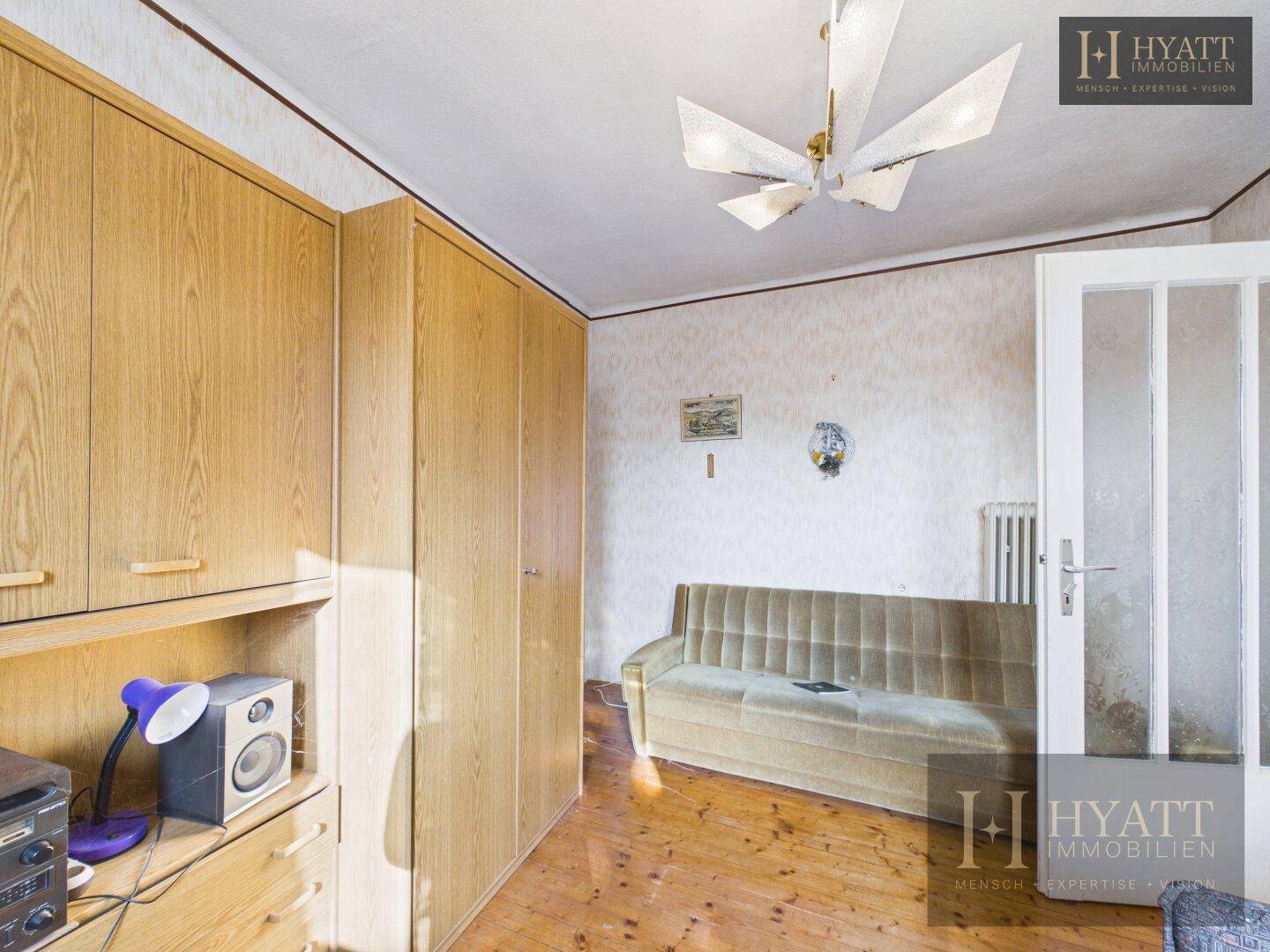 Zimmer mit Holzschränken, Sofa und Holzboden, das als Gäste- oder Kinderzimmer genutzt werden könnte.