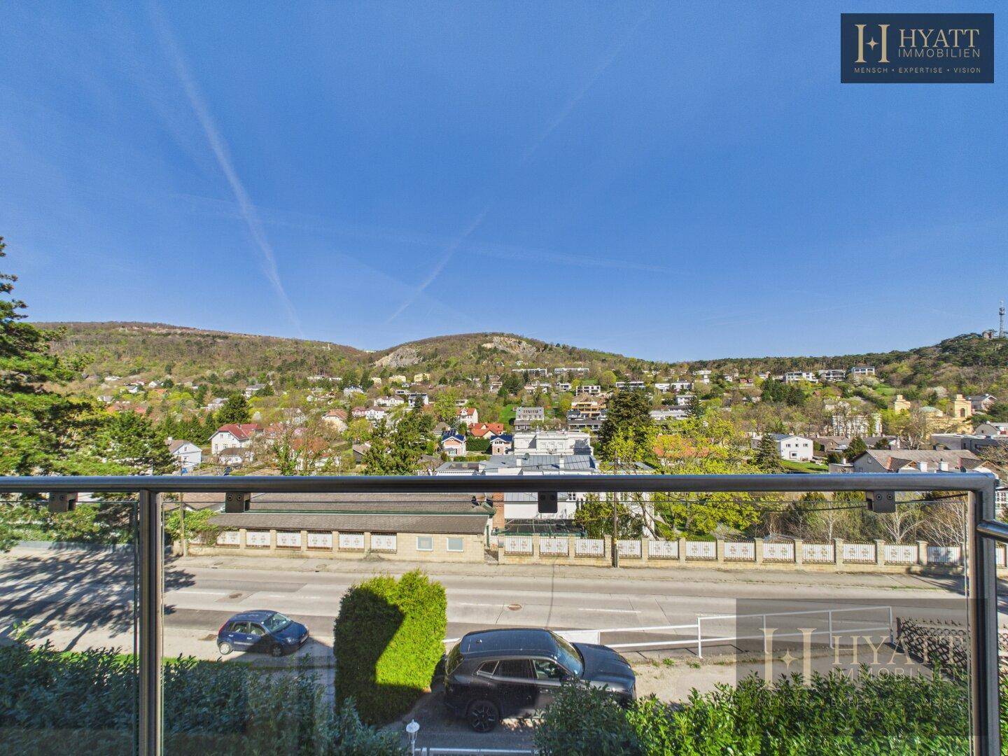 Panoramablick von einem Balkon auf eine hügelige Landschaft mit Häusern und einer Straße.