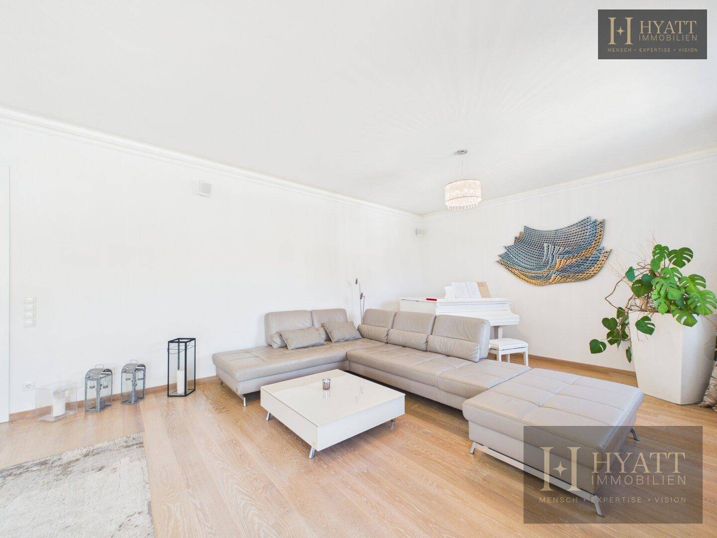 Modern eingerichtetes Wohnzimmer mit großem Ecksofa, weißem Flügel und stilvoller Dekoration.