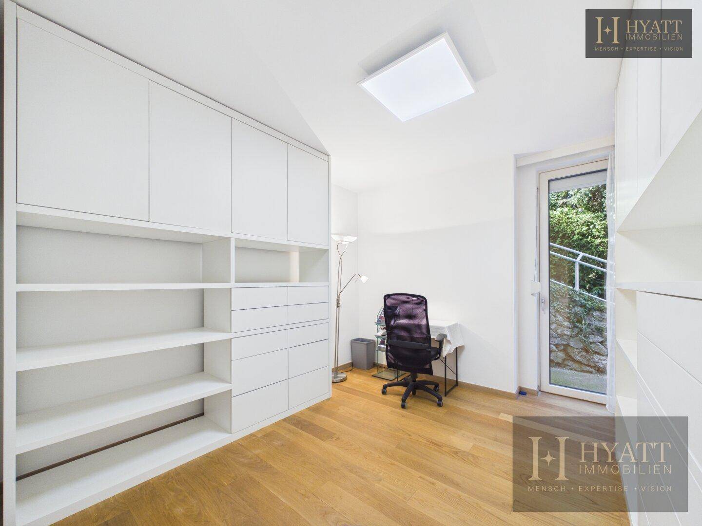 Helles Zimmer mit Einbauschränken, Schreibtisch und Zugang zum Außenbereich.
