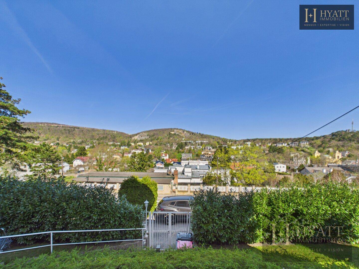 Weitläufiger Blick über eine grüne Hügellandschaft mit Häusern und viel Natur.