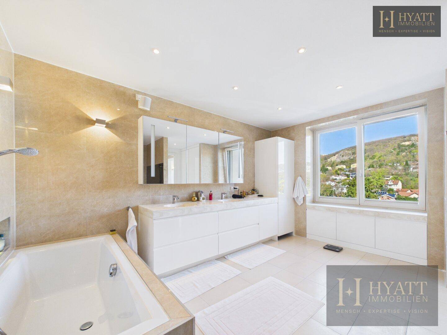 Helles Badezimmer mit Badewanne, Doppelwaschbecken und großem Fenster mit Weitblick.