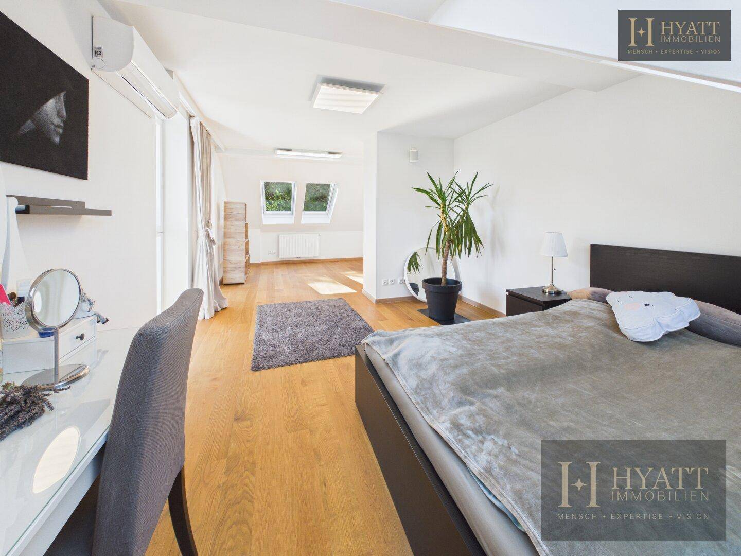 Helles Schlafzimmer im Dachgeschoss mit Bett, Schminktisch und Blick durch Dachfenster.