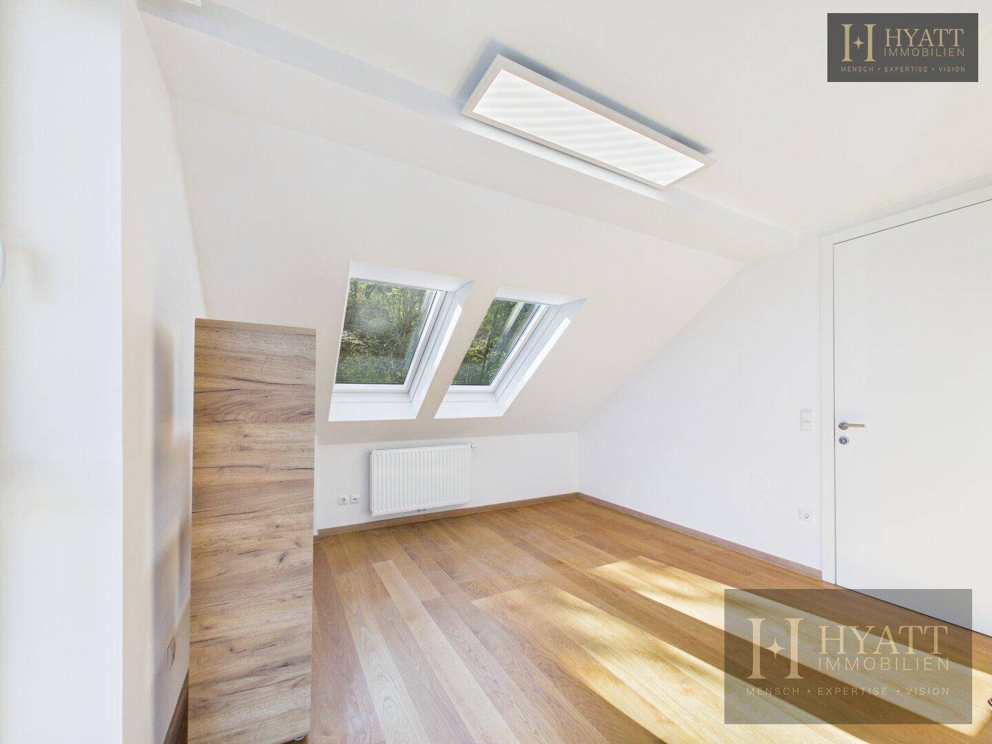 Leeres Dachzimmer mit Dachschrägen, zwei Dachfenstern und Heizkörper.