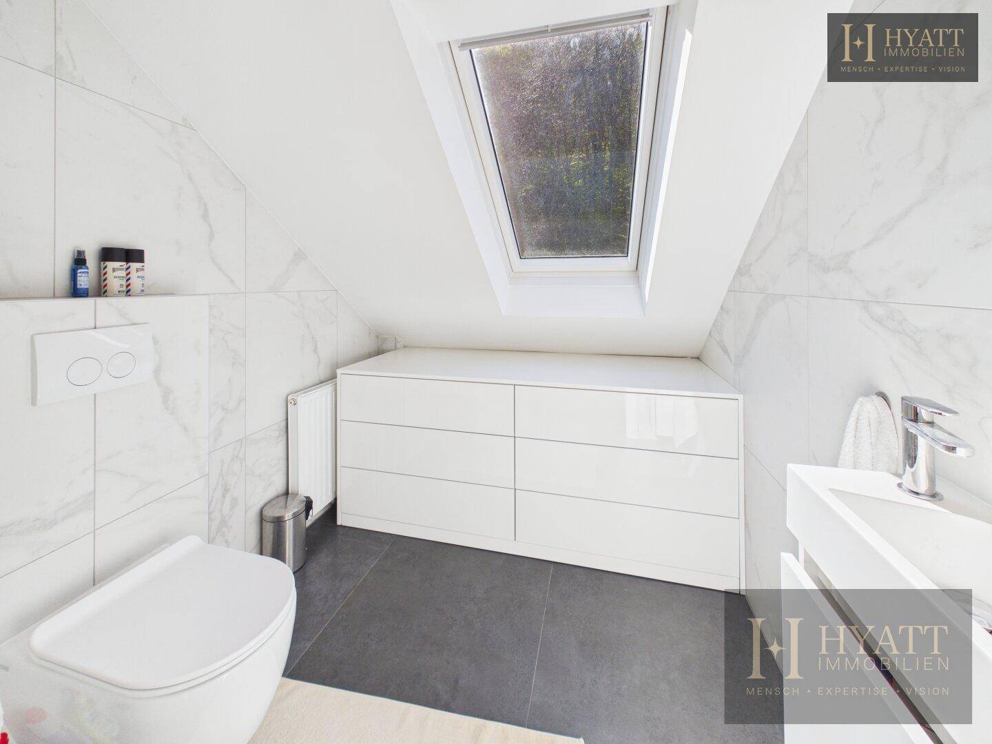 Modernes Badezimmer im Dachgeschoss mit WC, Waschtisch, Dachfenster und eleganten Fliesen.