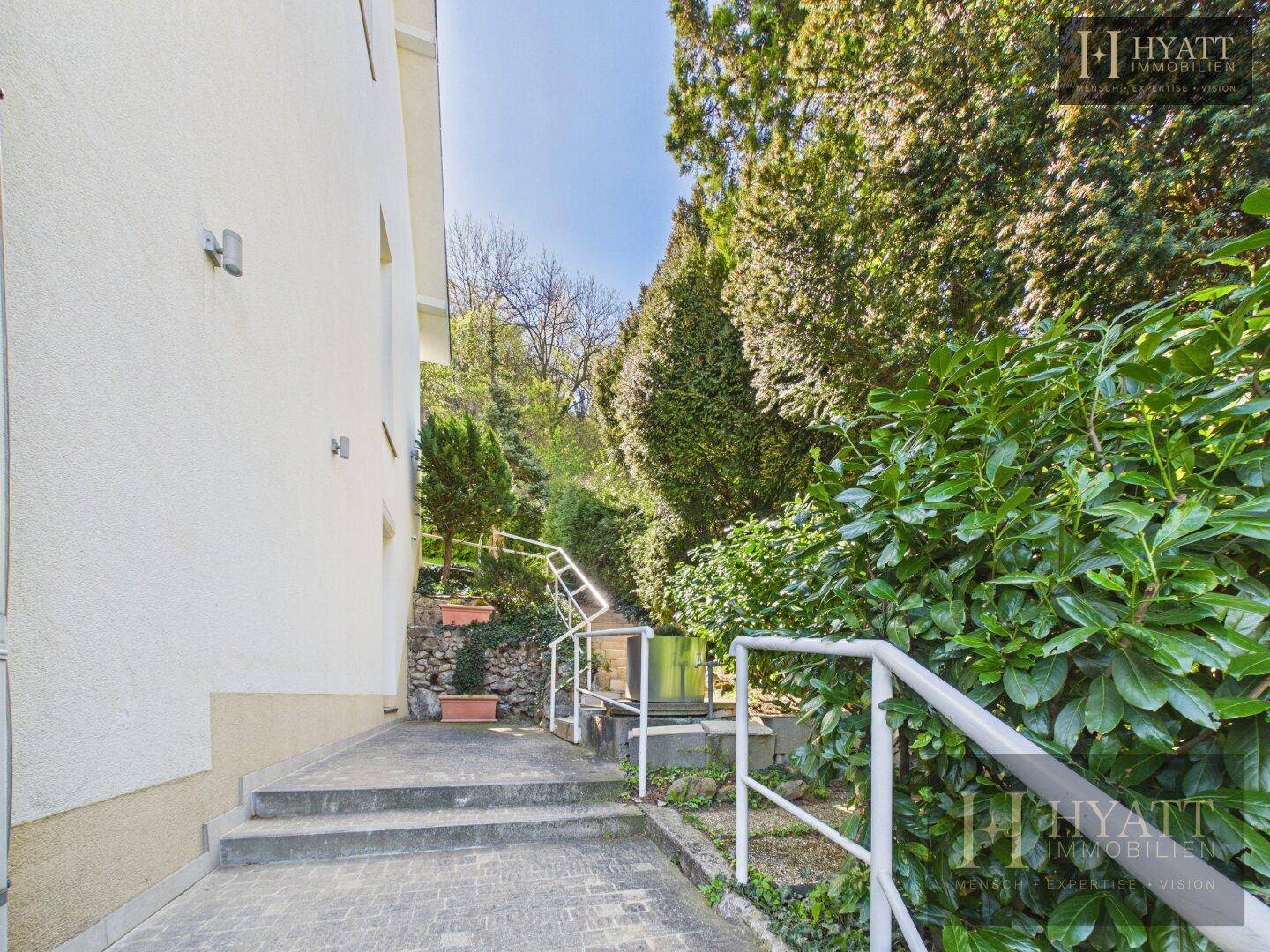 Zugangsweg mit Treppen und Rampe, umgeben von üppiger Vegetation.