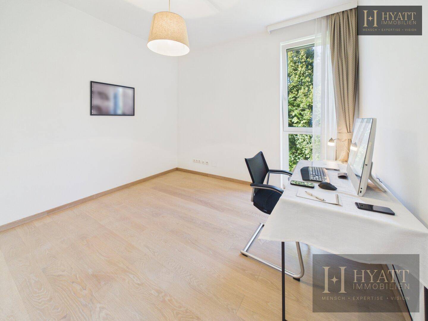 Helles Arbeitszimmer mit Schreibtisch, Computer und großem Fenster mit Blick ins Grüne.