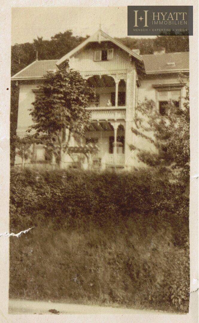 Historisches Gebäude im Sepia-Ton, umgeben von üppiger Vegetation, mit traditioneller Architektur.