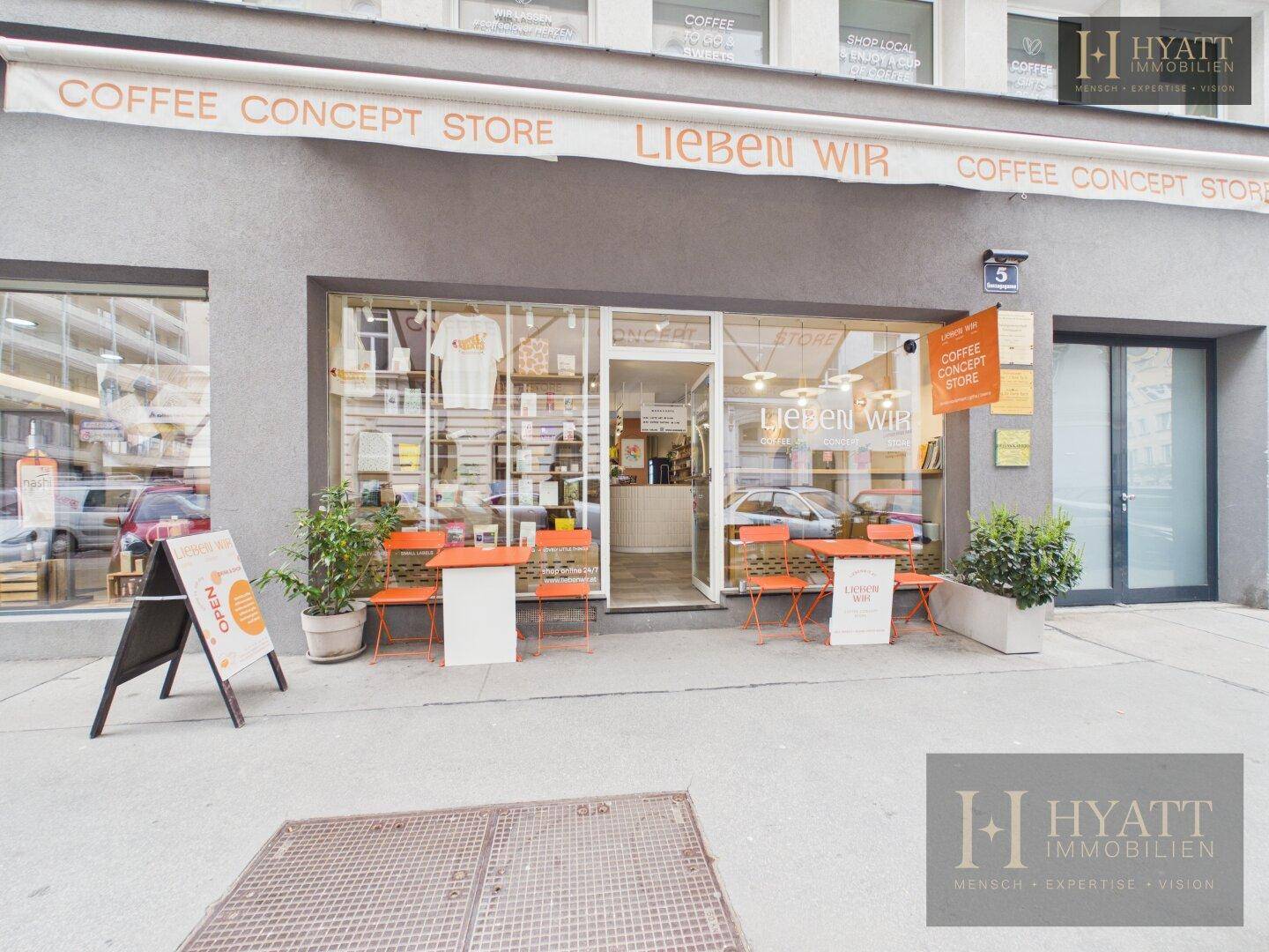 Außenansicht eines modernen Concept Stores mit Markise, großen Schaufenstern und Außensitzplätzen.