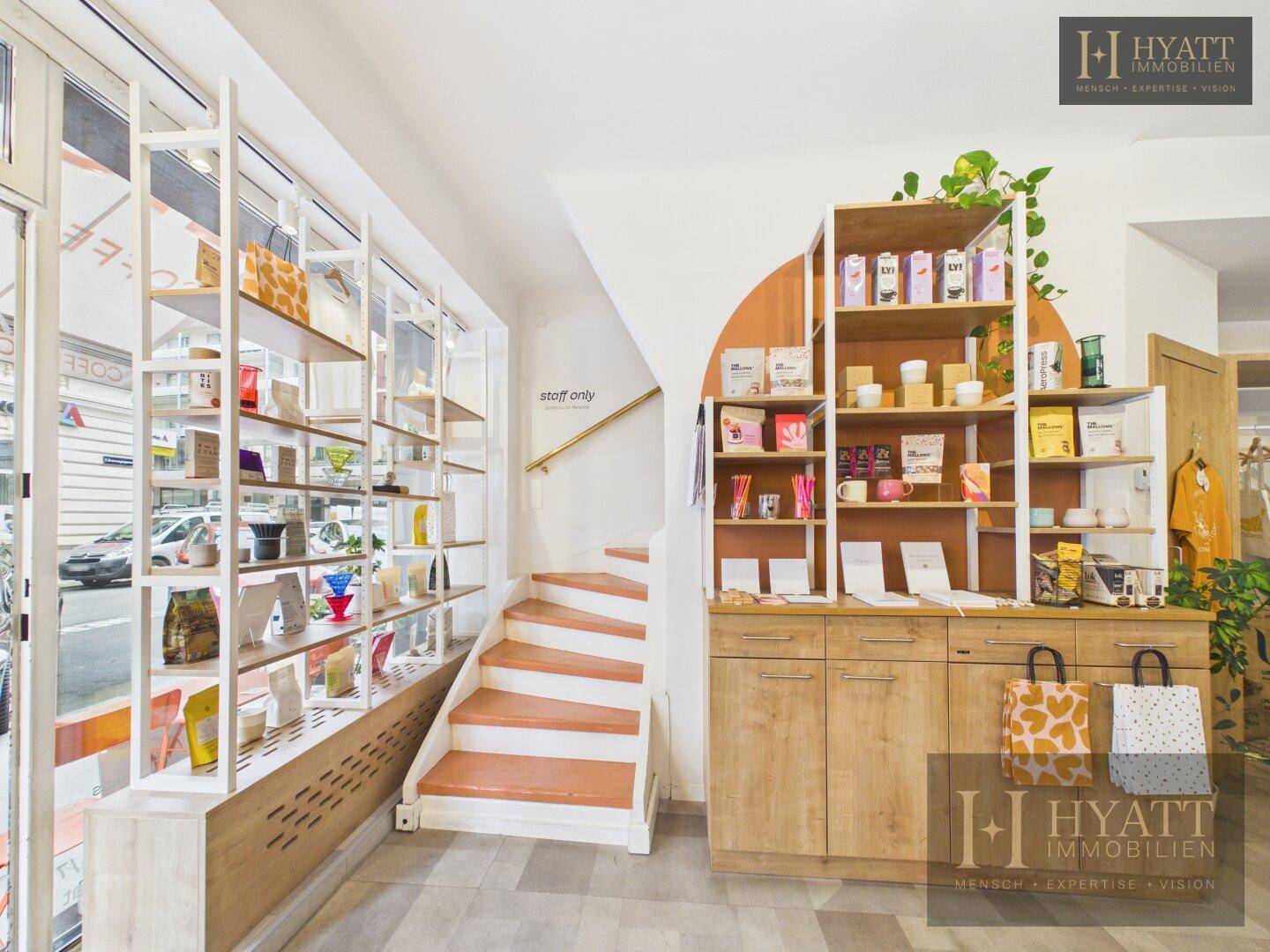 Innenansicht eines Concept Stores mit Verkaufsregalen, einer Treppe und großen Schaufenstern zur Straße.