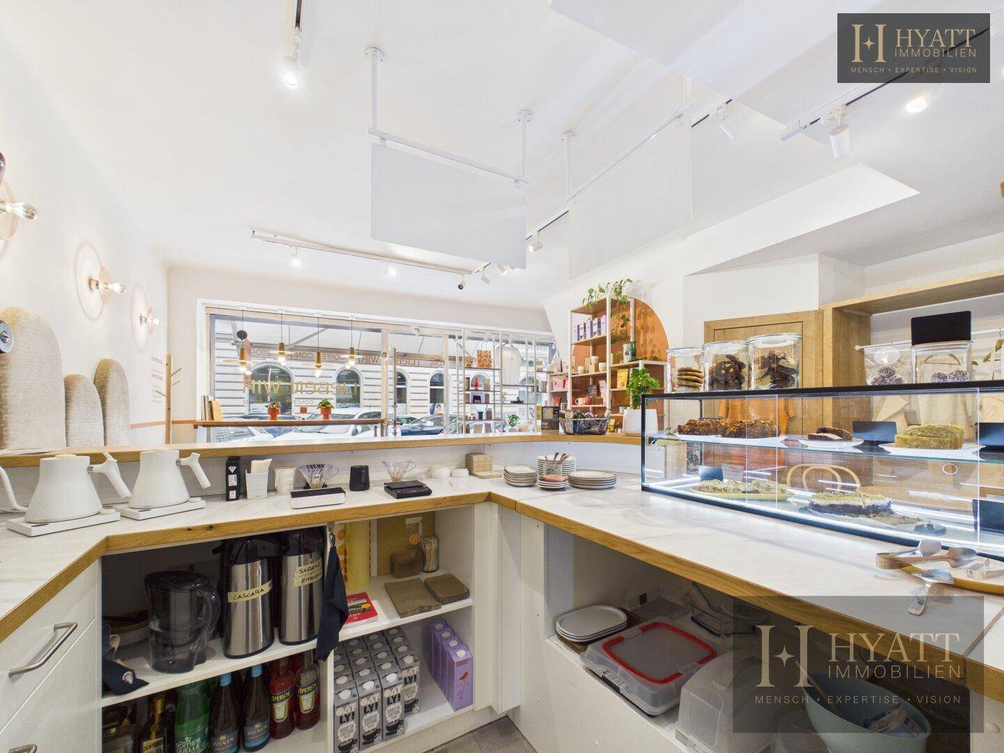Thekenbereich mit Getränken, Kaffeemaschinen und einem Kuchenschrank in einem Concept Store.