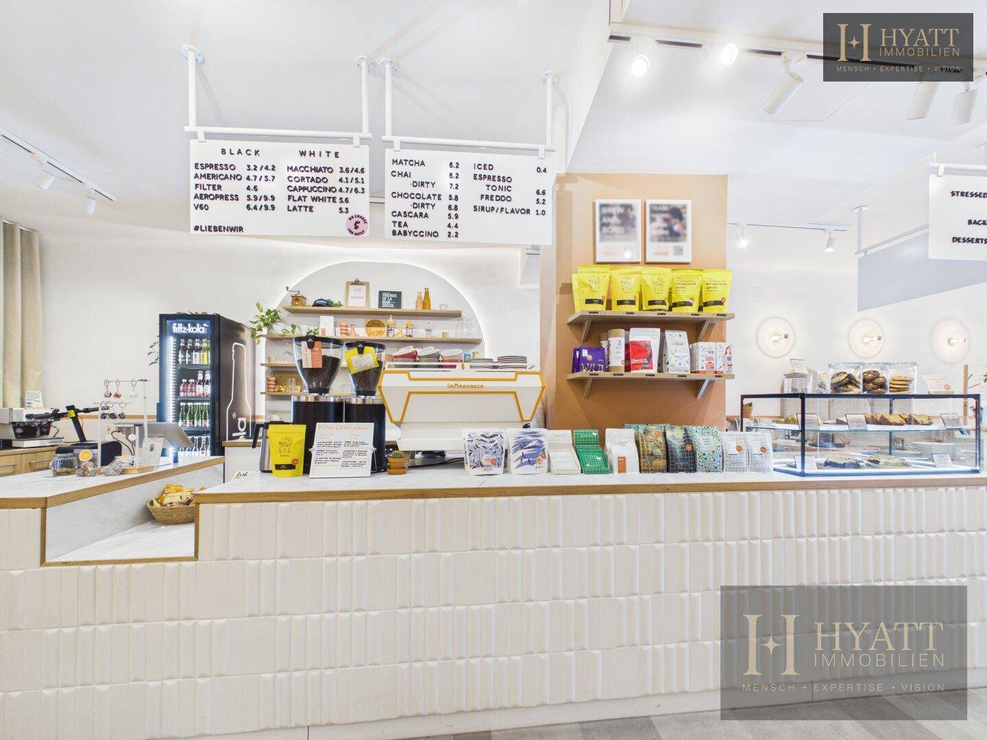 Haupttheke eines Concept Stores mit Kaffeebar, Preistafel und Produkten in hellem Ambiente.