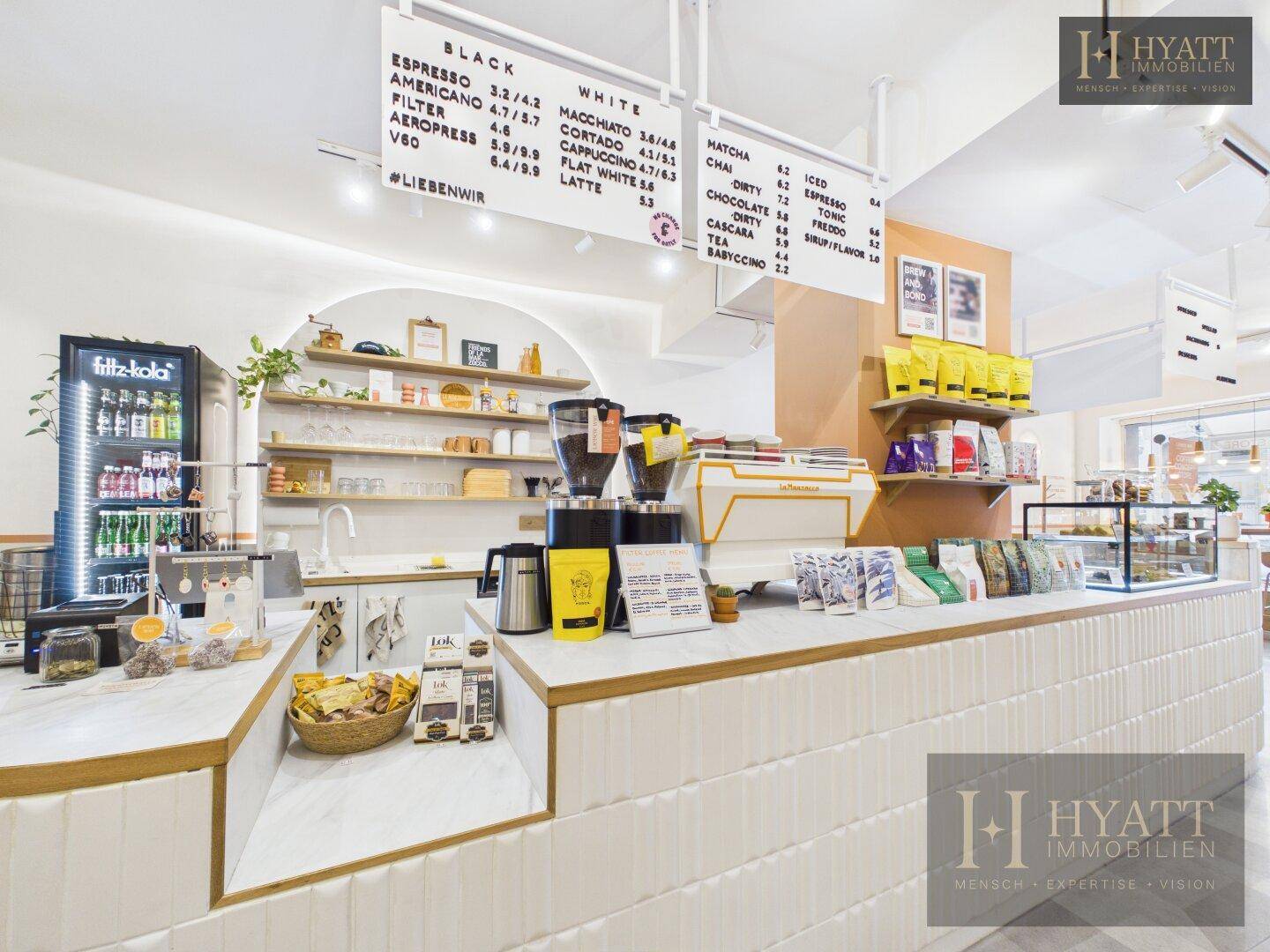 Kaffeebar mit professionellen Maschinen, Getränkekühlschrank und Preistafel in einem Concept Store.