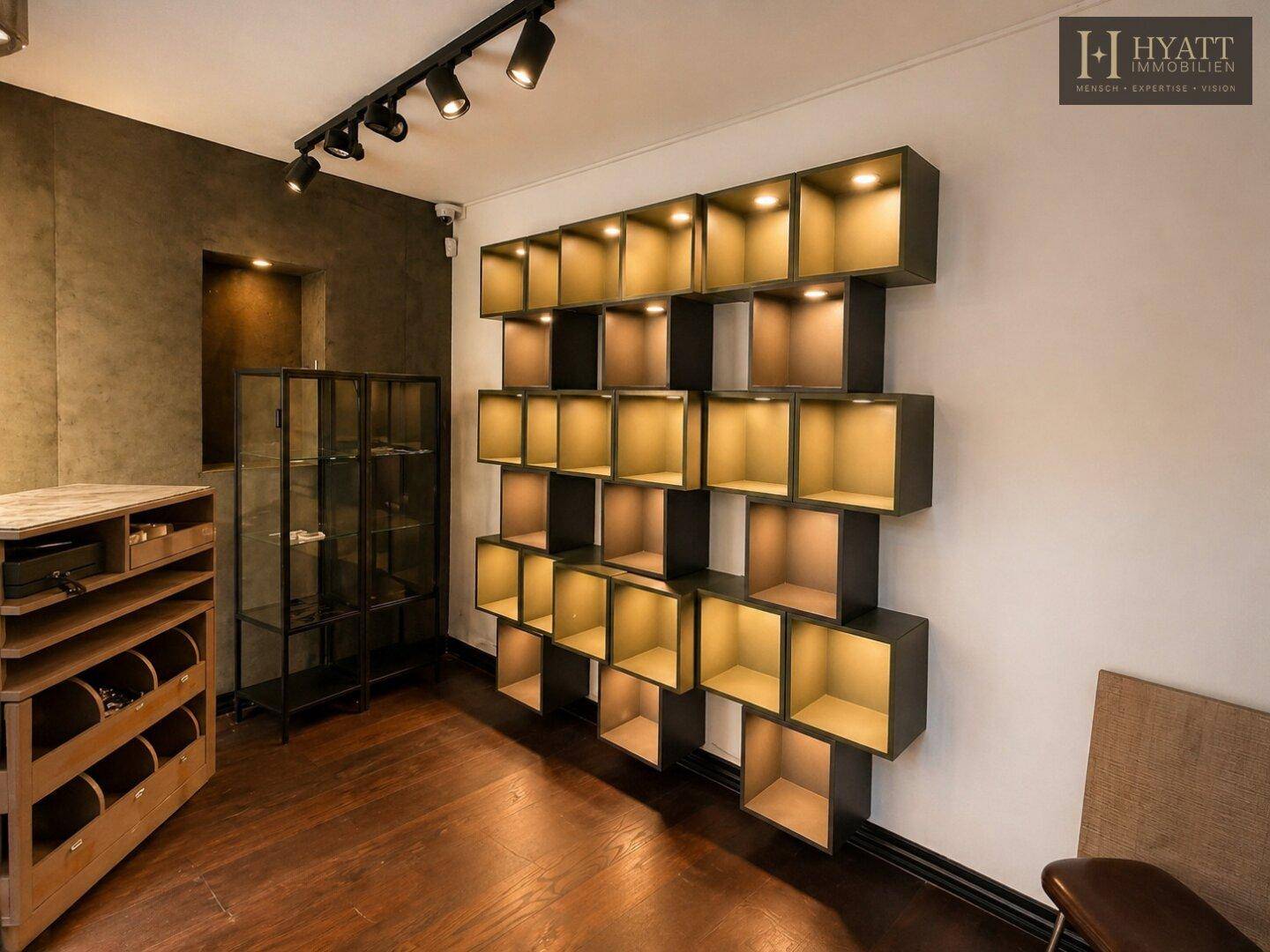 Innenansicht eines modernen Ladenlokals mit Holzboden und beleuchteten Präsentationsregalen an der Wand.