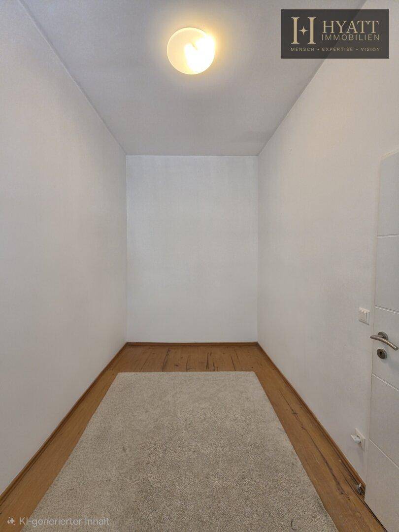 Kleiner, leerer Raum mit Holzboden und Teppich, beleuchtet von einer Deckenleuchte.