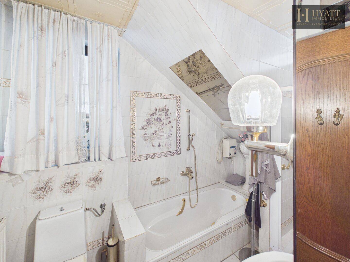 Helles Badezimmer im Dachgeschoss mit Badewanne, Fliesen und Dachfenster.