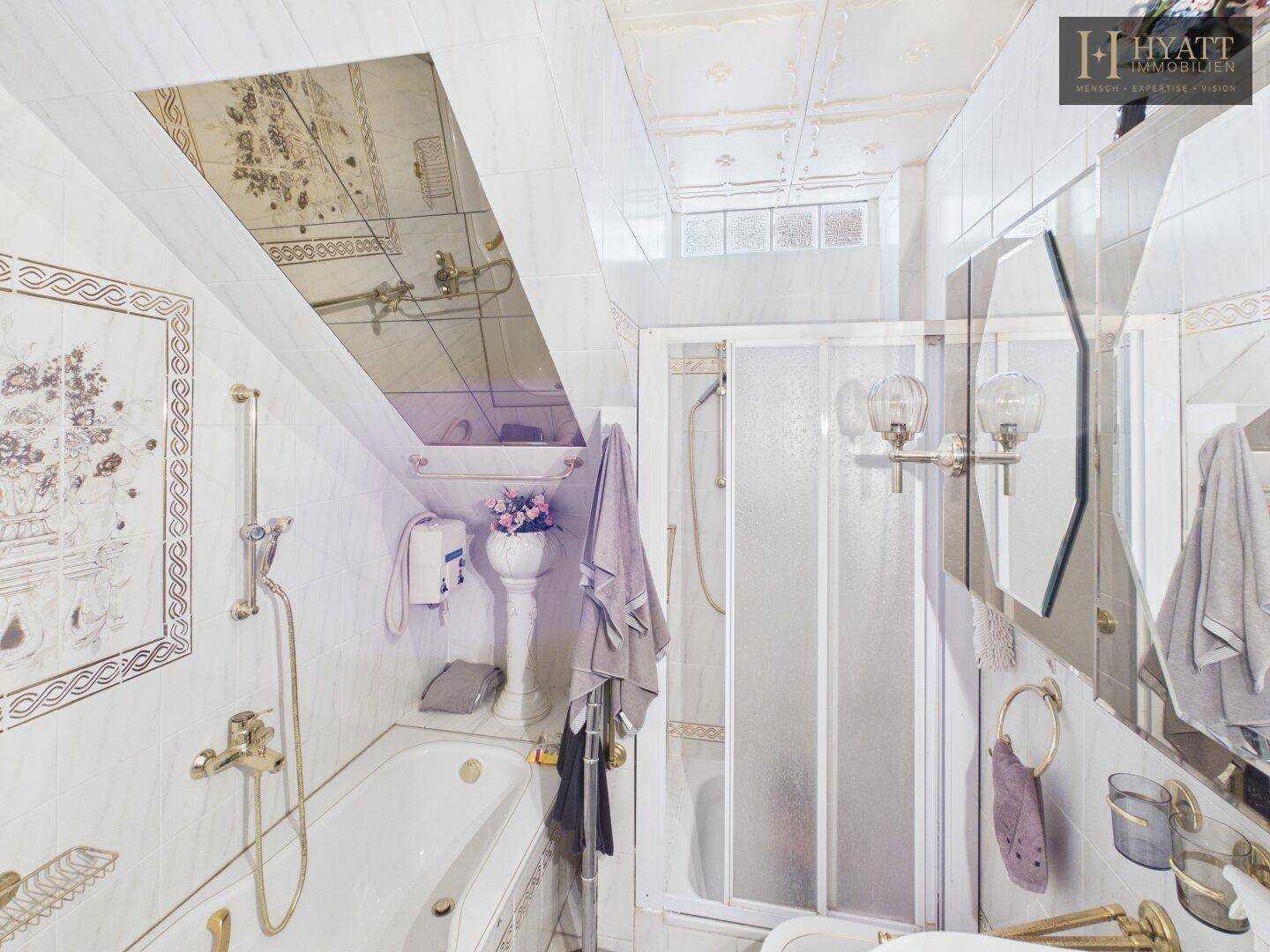 Badezimmer mit Badewanne, Duschkabine und Dachschräge, hell gefliest.