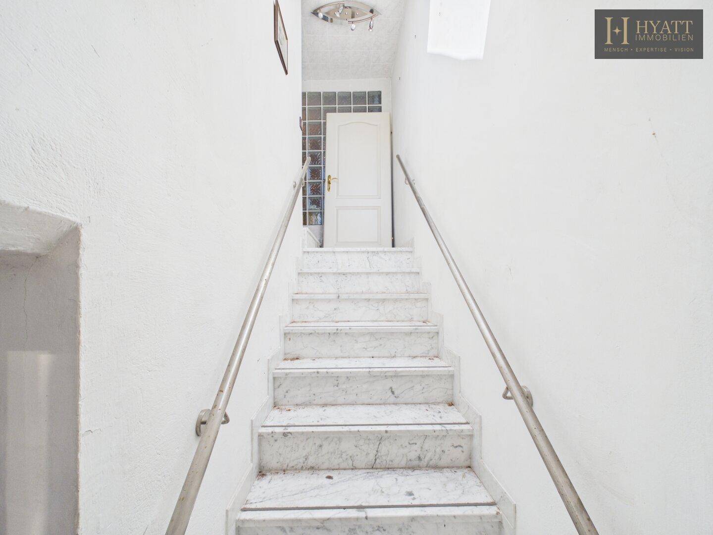 Marmortreppe mit Geländer führt zu einem oberen Stockwerk in hellem Ambiente.
