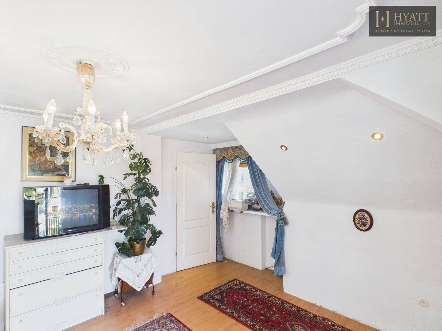 Geräumiges Zimmer mit Holzboden, Dachschräge und Kronleuchter.