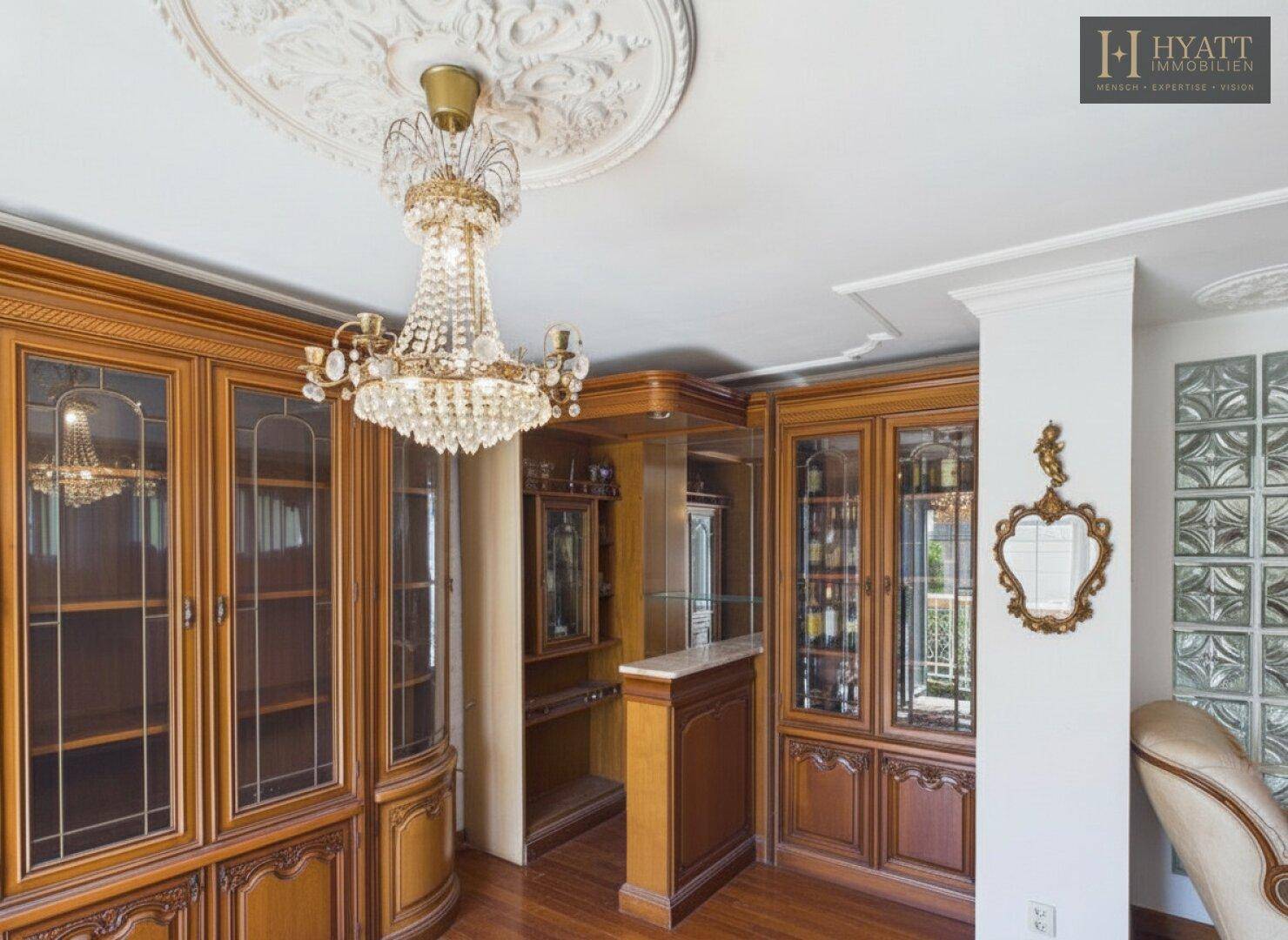 Elegantes Wohnzimmer mit reich verzierten Holzschränken, Kronleuchter und Stuckdecke.