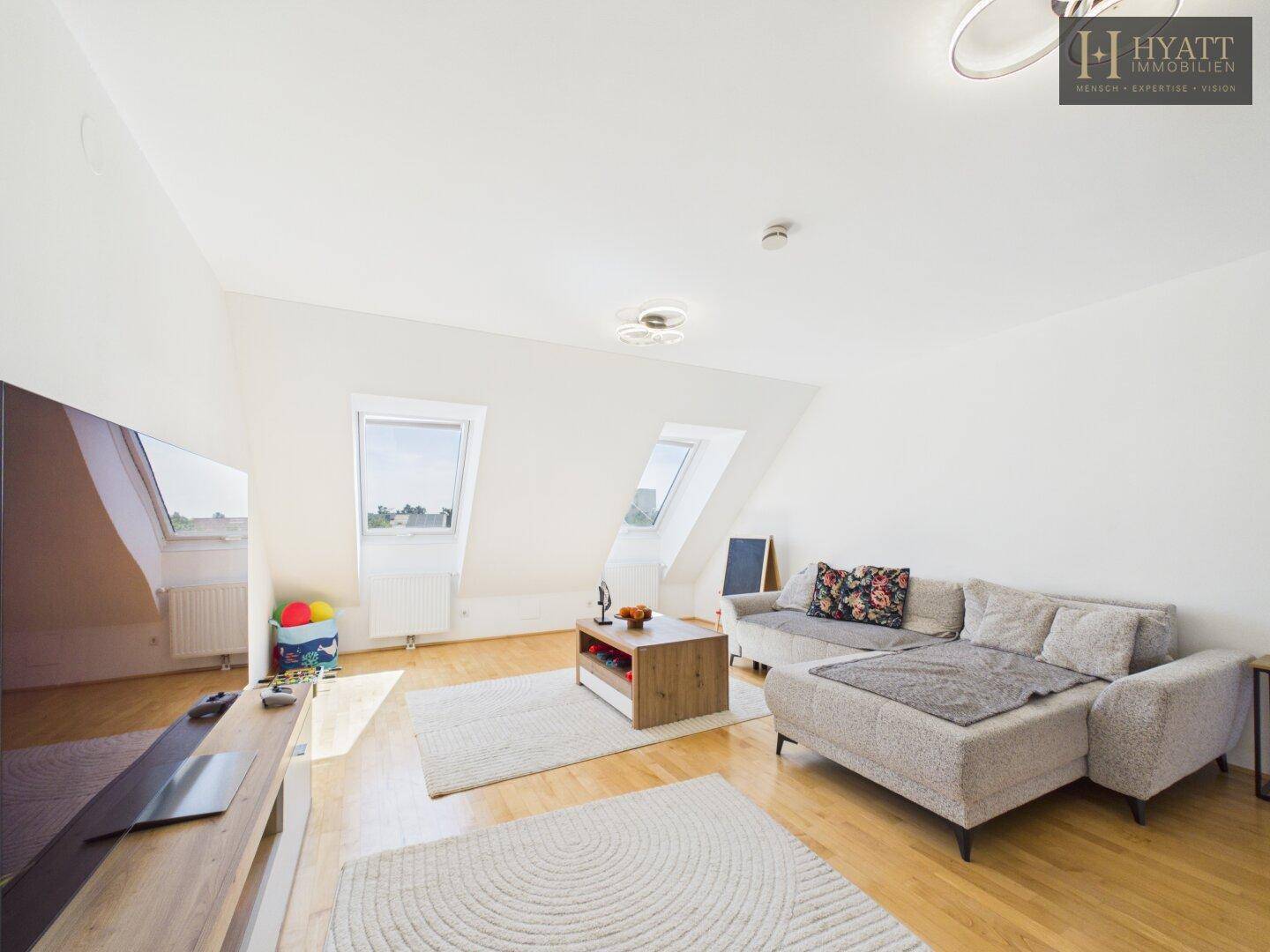 Gemütlicher Wohnbereich mit Dachfenstern, Holzboden und großem Ecksofa.