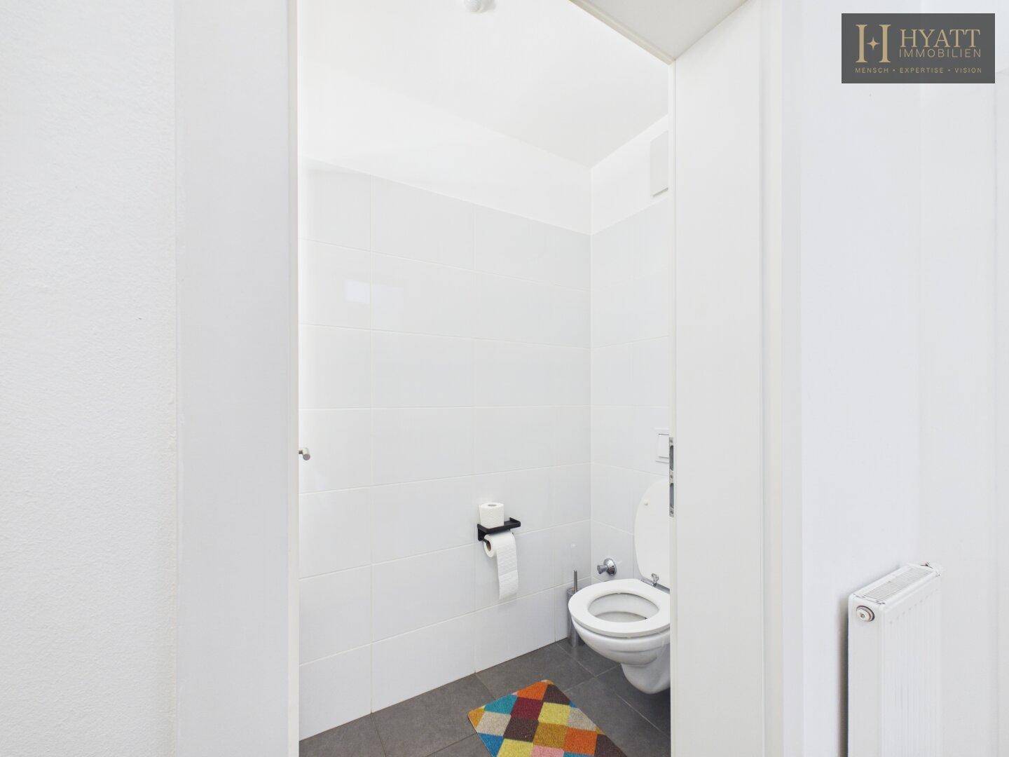 Schlichtes Gäste-WC mit weiß gefliesten Wänden und farbigem Teppich.