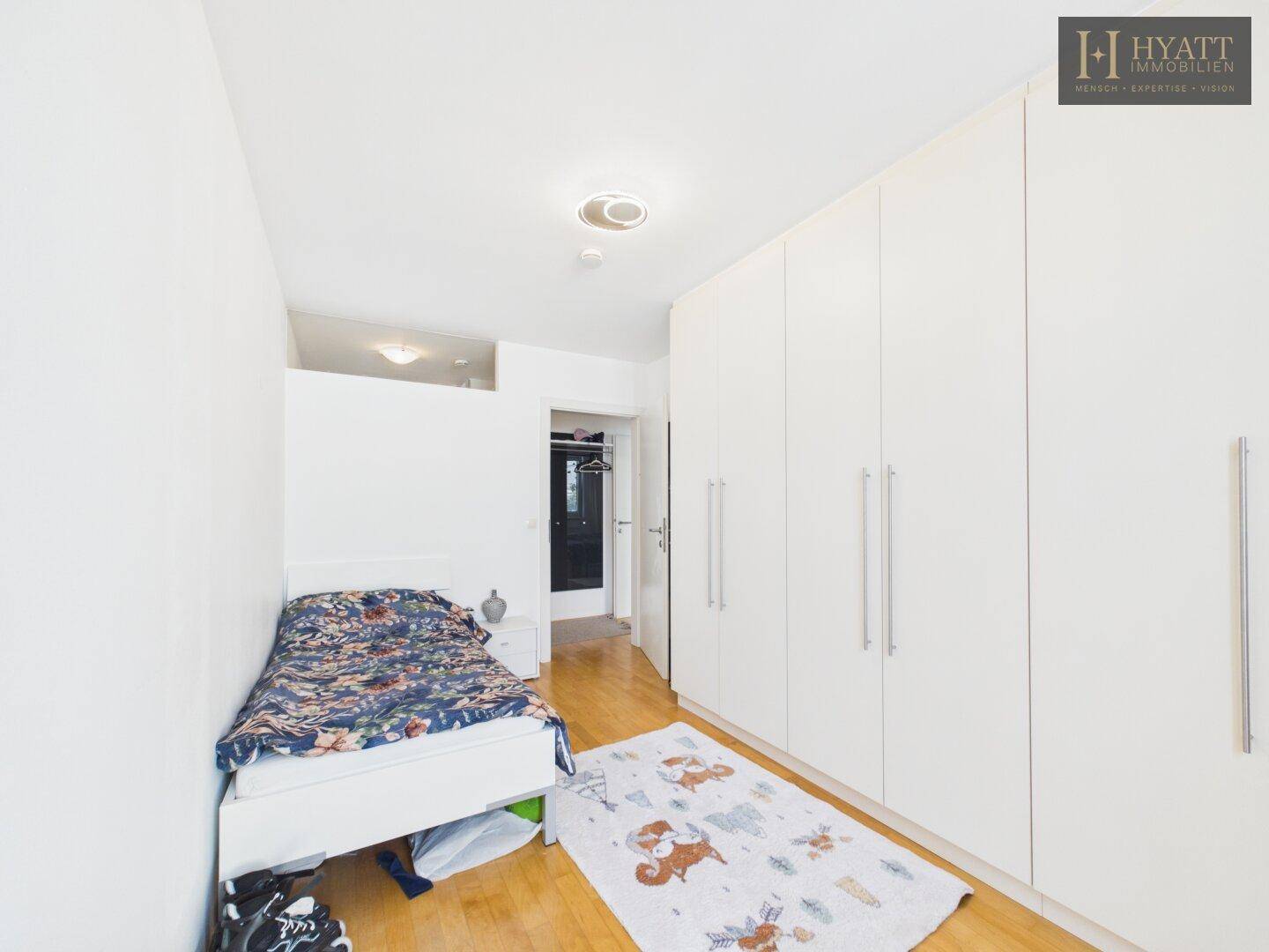 Schlafzimmer mit Einzelbett, Einbauschränken und Holzboden.