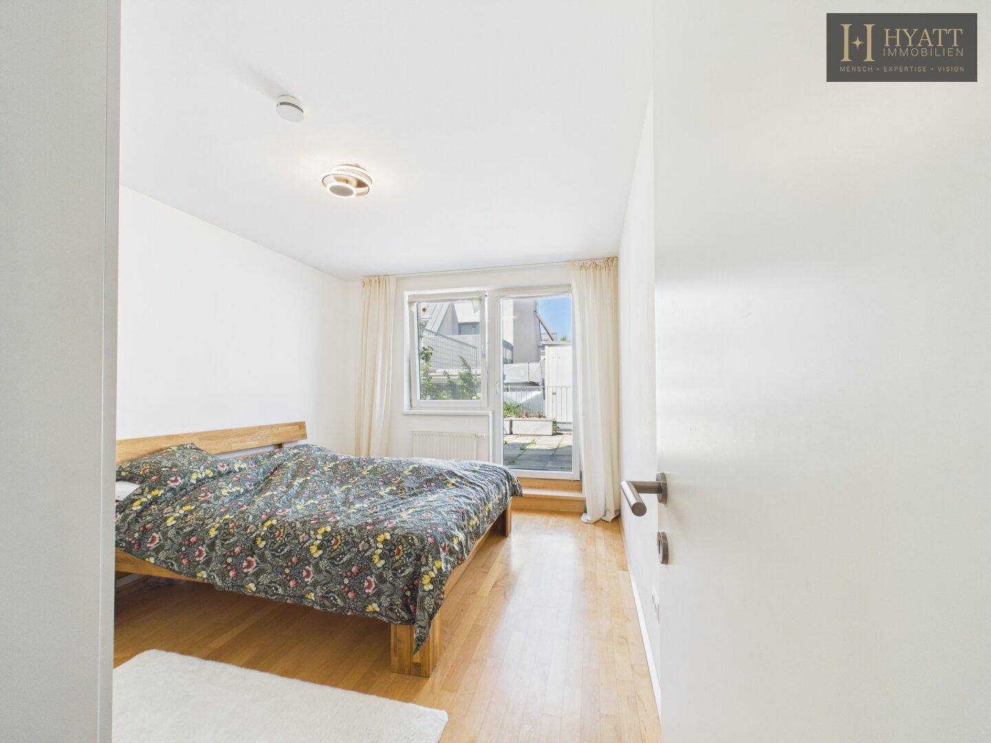 Helles Schlafzimmer mit Doppelbett, Holzboden und Zugang zu einem Balkon.