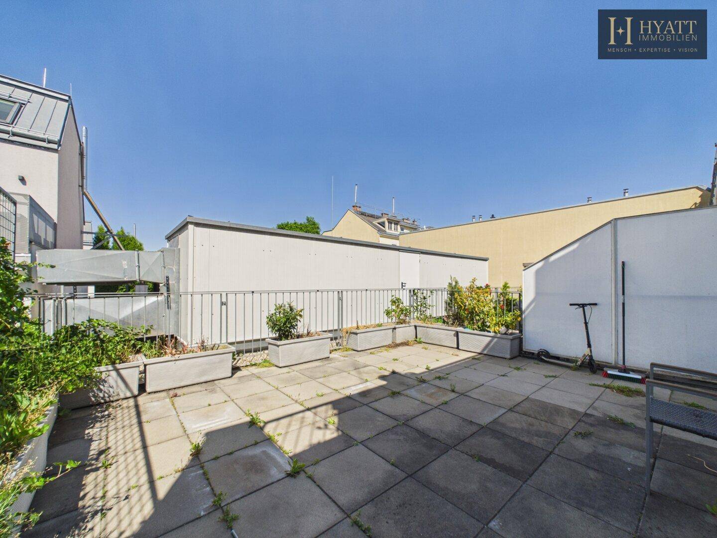 Große Dachterrasse mit Steinplatten, Pflanzkübeln und Blick auf die Umgebung.