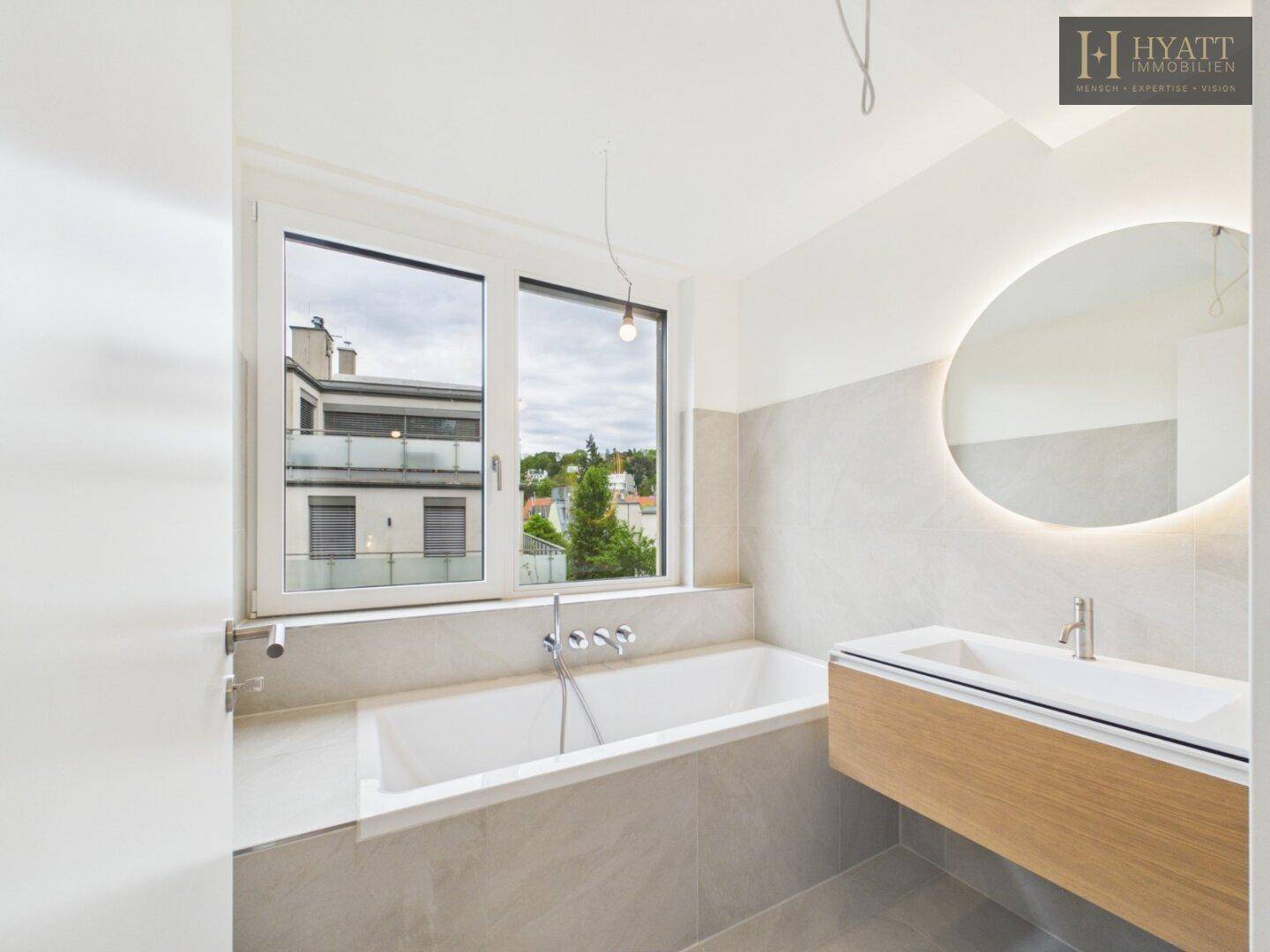 Modernes Badezimmer mit Badewanne, stilvollem Waschtisch und beleuchtetem Spiegel sowie Fenster.