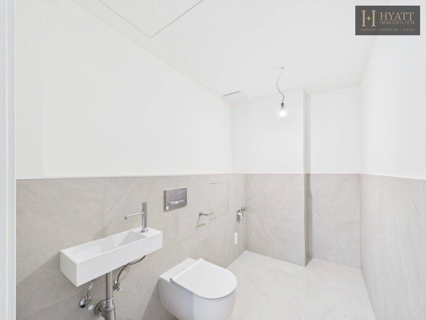 Modernes Gäste-WC mit wandhängender Toilette, kleinem Waschbecken und hellen Fliesen.