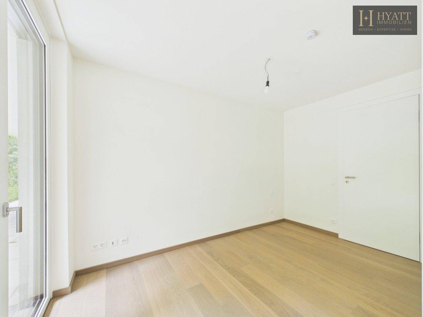 Helles Zimmer mit Holzboden und großem Fenster, das viel Tageslicht hereinlässt.
