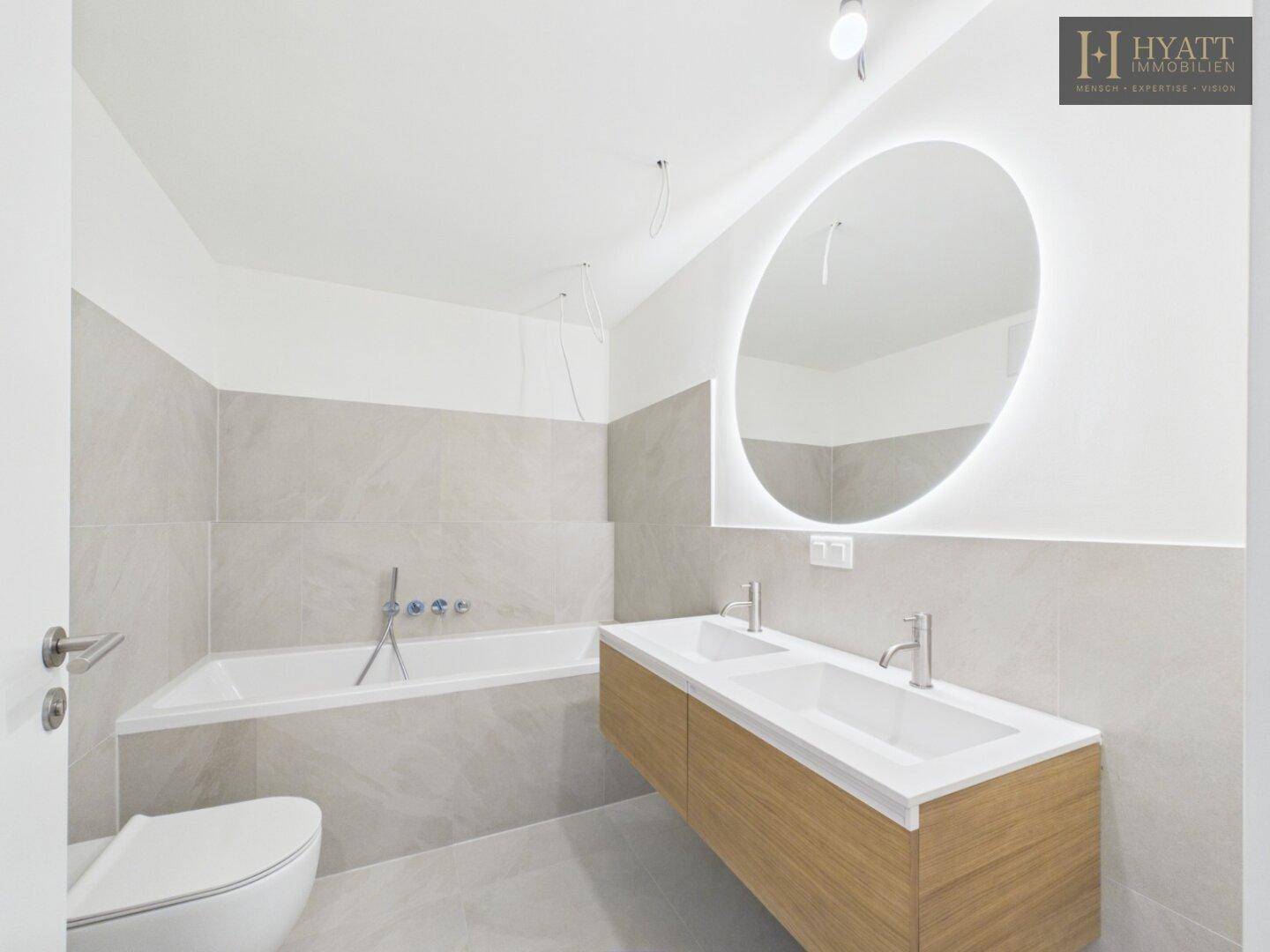 Modernes Badezimmer mit Badewanne, Doppelwaschbecken und großem beleuchteten Spiegel.