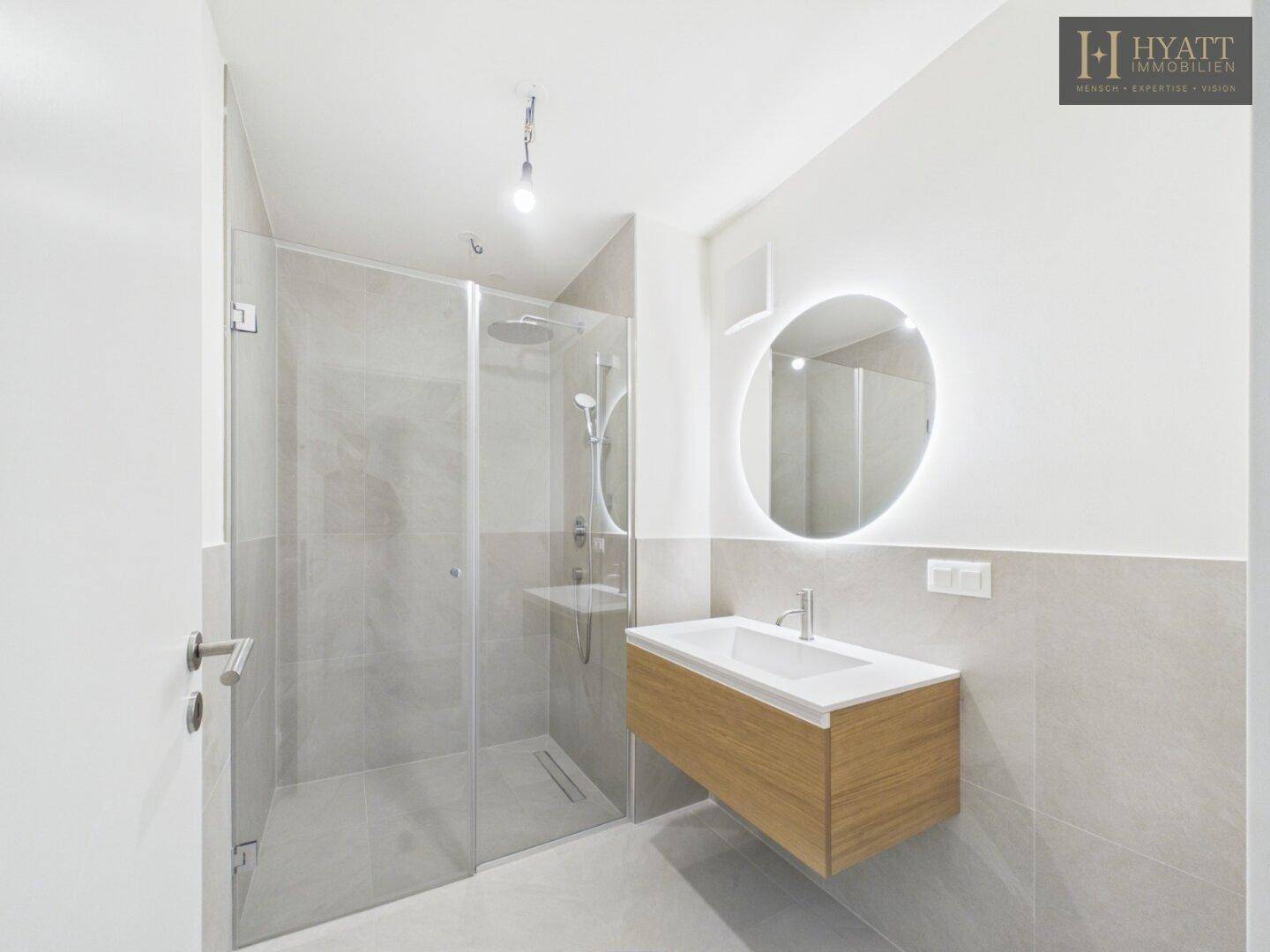 Modernes Badezimmer mit begehbarer Dusche, elegantem Waschtisch und beleuchtetem Spiegel.