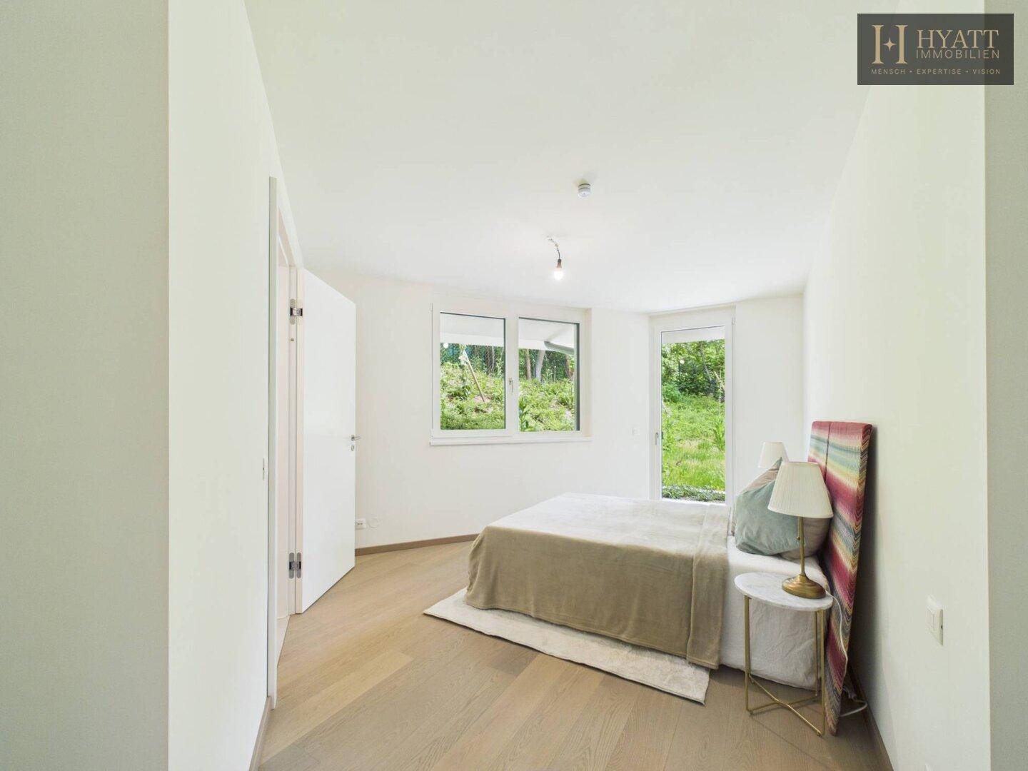 Geräumiges Schlafzimmer mit Holzboden, großem Fenster und Blick auf die grüne Umgebung.
