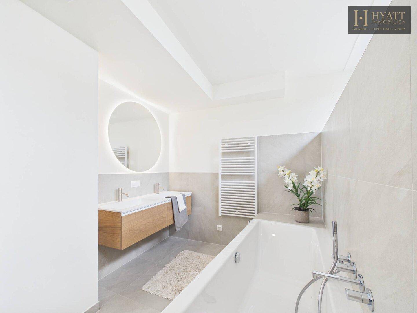 Elegantes Badezimmer mit Doppelwaschbecken, beleuchtetem Spiegel und Badewanne.