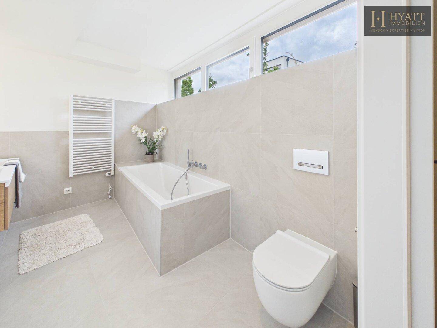 Modernes Badezimmer mit Badewanne, Wand-WC, Handtuchheizkörper und Fenster.