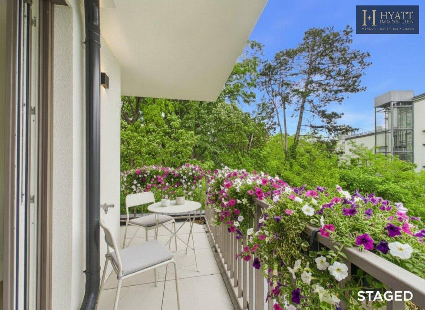 Blühender Balkon mit Sitzgelegenheiten und üppigem Grünblick, ideal zum Entspannen im Freien.