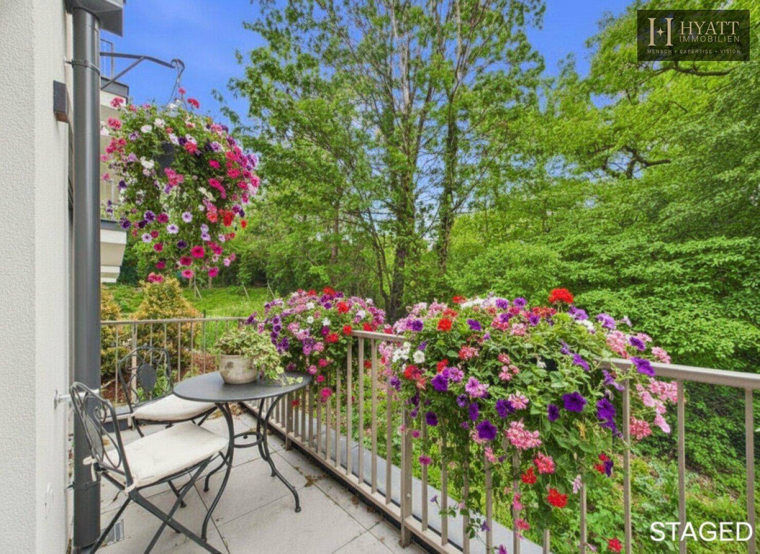 Dekorierter Balkon mit bunten Blumen, Sitzgelegenheiten und einem schönen Blick ins Grüne.