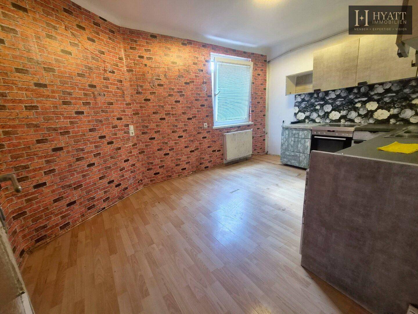 Leere Küche mit Holzboden und Ziegelstein-Tapete, bereit für neue Einbauten.