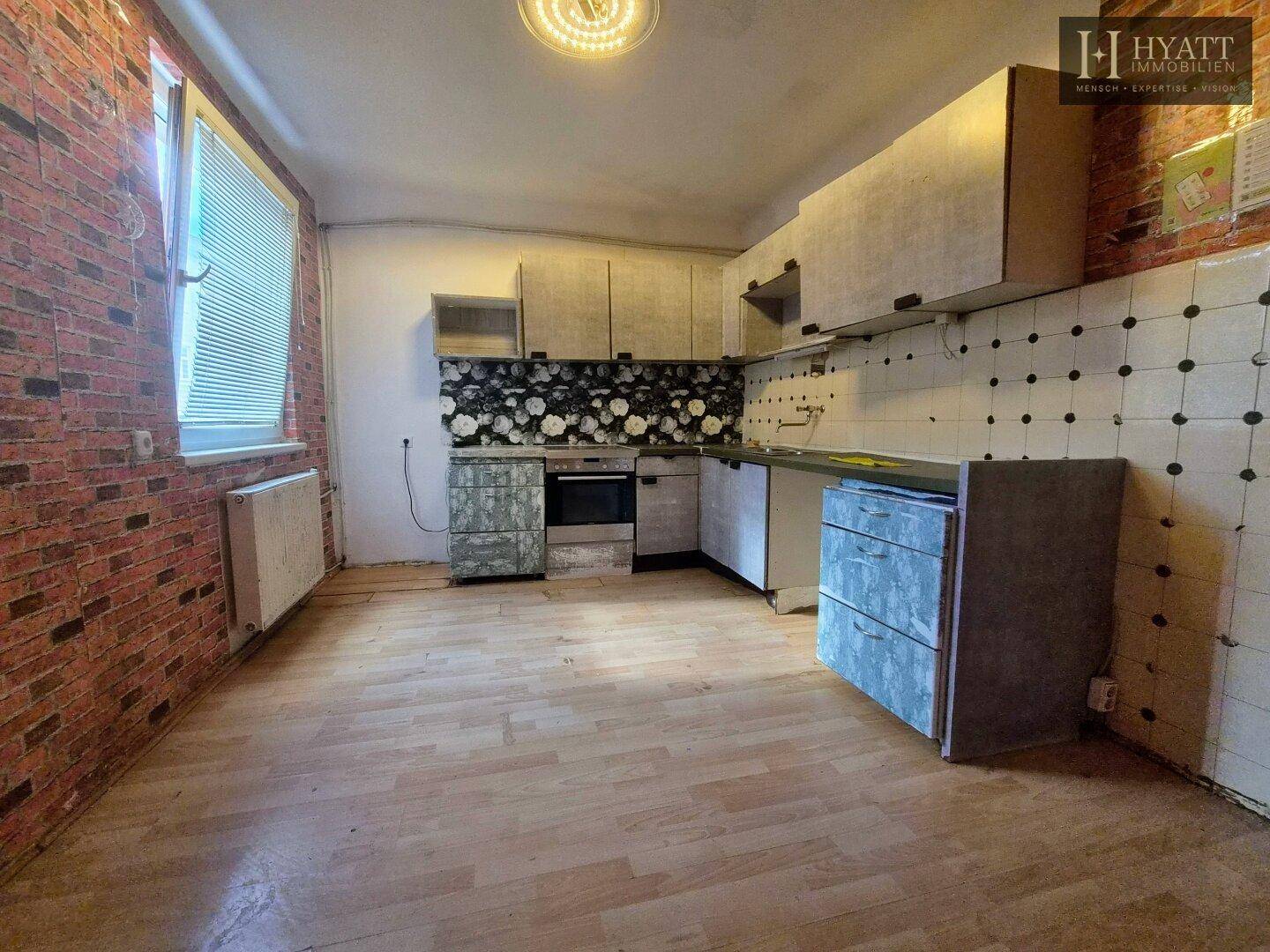 Leere Küche mit Holzboden und Ziegelstein-Tapete, bereit für neue Küchenmöbel.