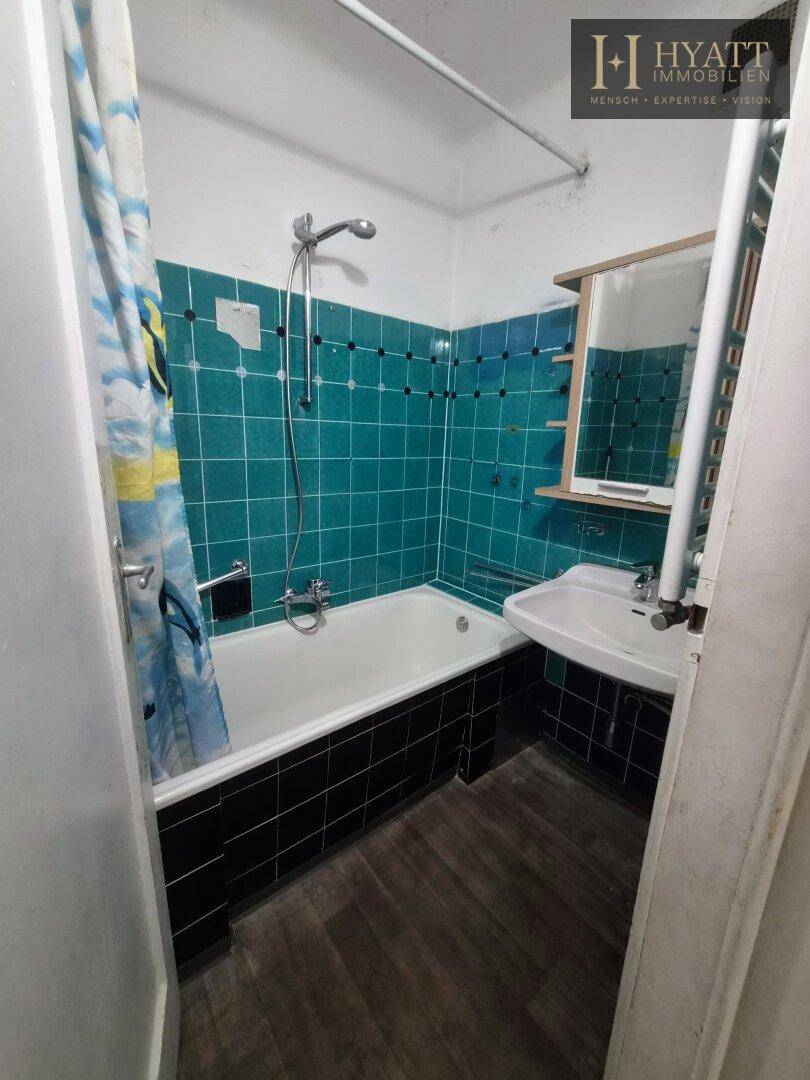 Badezimmer mit Badewanne und Duschvorhang, türkisfarbenen Fliesen und dunklem Boden.