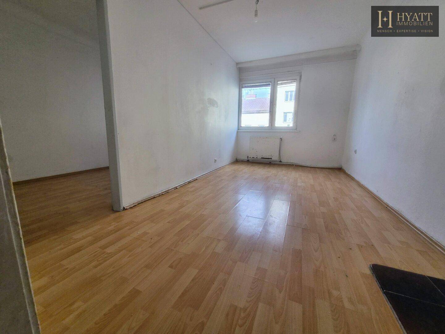 Helles Wohnzimmer mit Holzboden und Fenster, bereit zur individuellen Einrichtung.