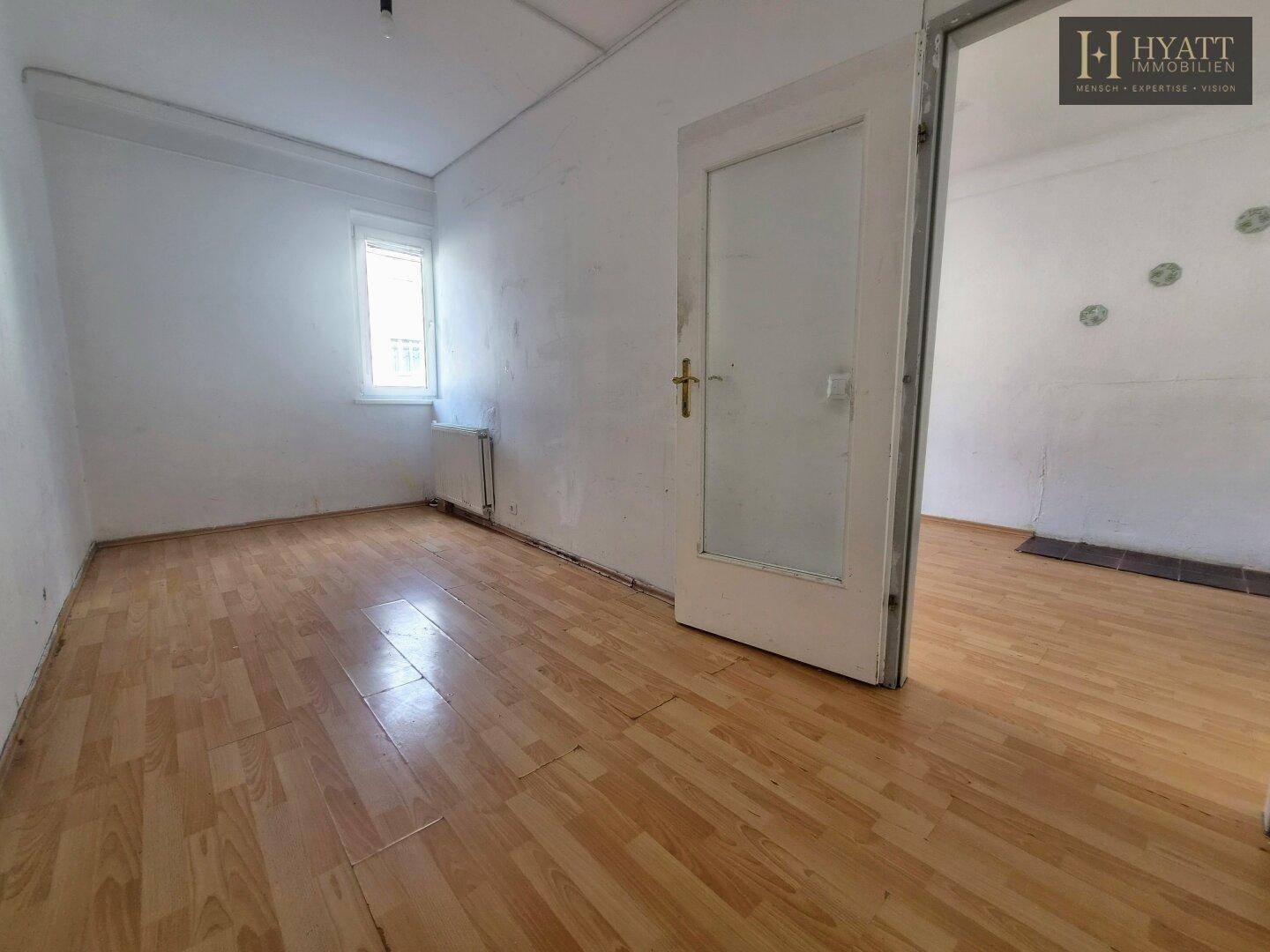 Geräumiges Wohnzimmer mit Holzboden und weiß gestrichenen Wänden, mit viel Tageslicht.