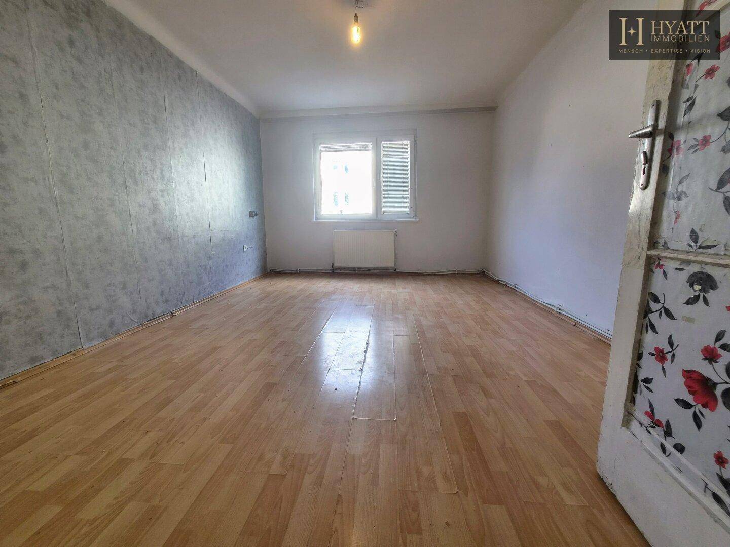 Helles Wohnzimmer mit Holzboden und grauer Akzentwand, mit Fenster für Tageslicht.