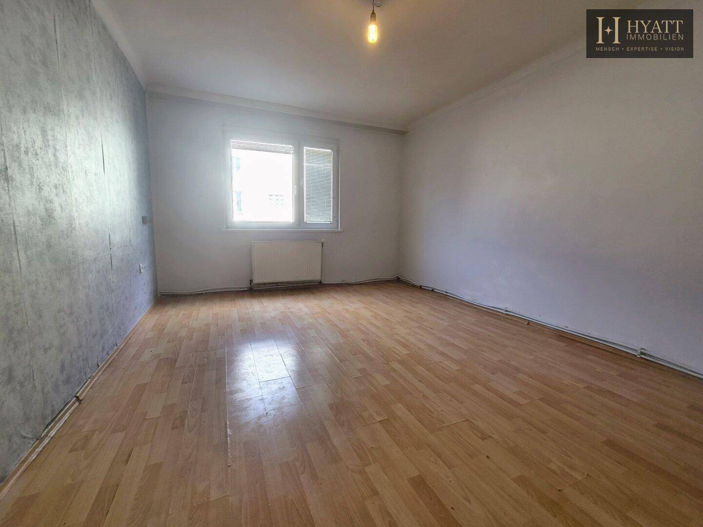 Geräumiges Wohnzimmer mit Holzboden und grauer Akzentwand, mit viel Tageslicht.