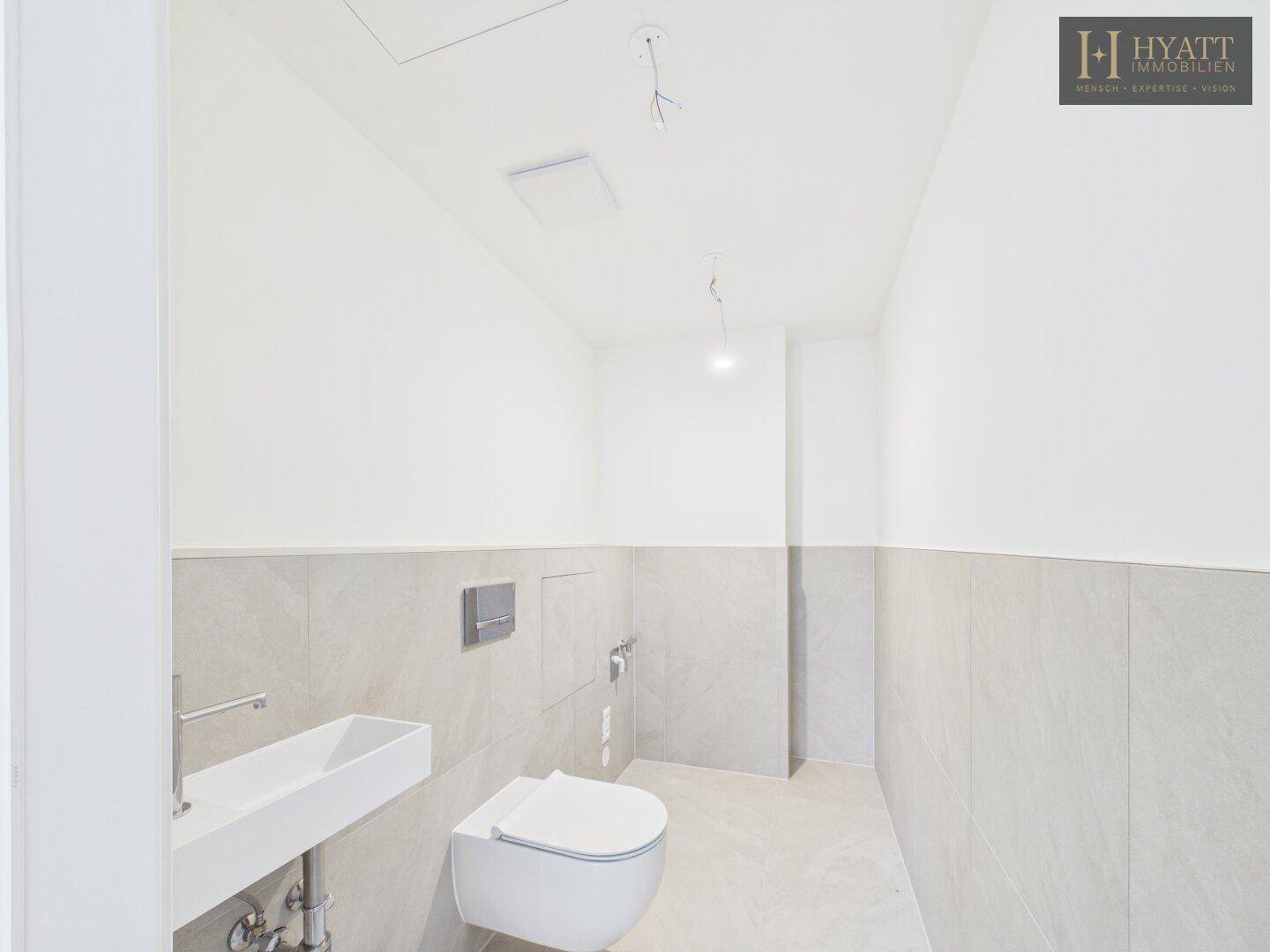 Modernes Gäste-WC mit wandhängendem WC, kleinem Waschbecken und Fliesen.