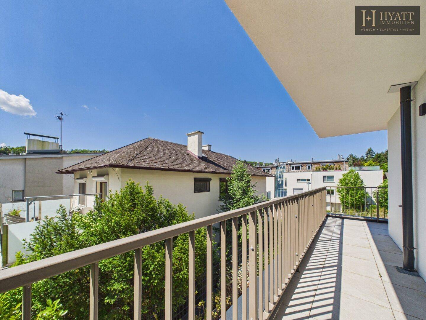Langer, sonniger Balkon mit Metallgeländer und weitem Blick ins Grüne.