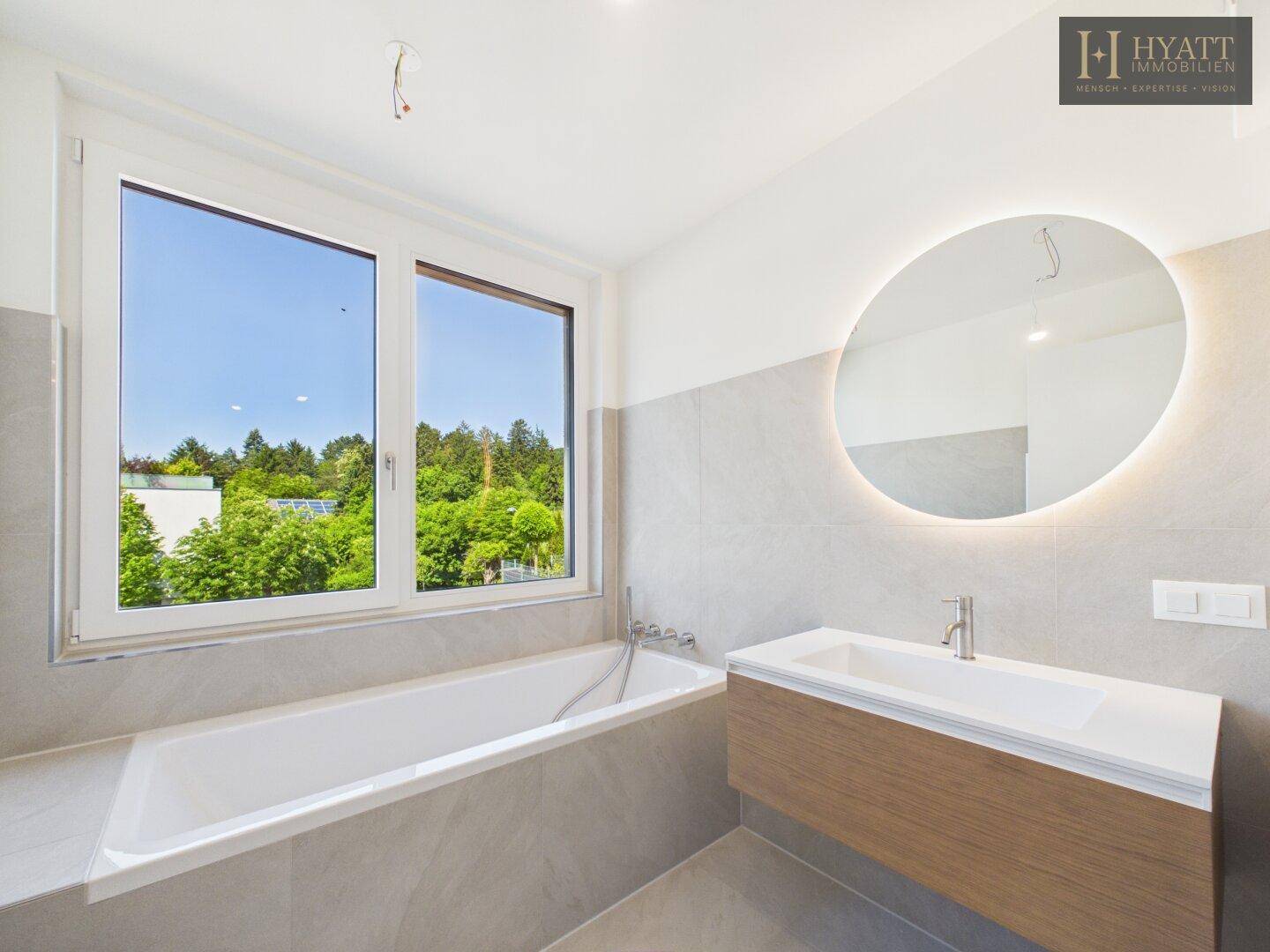 Modernes Badezimmer mit Badewanne, großem Fenster und Blick ins Grüne.