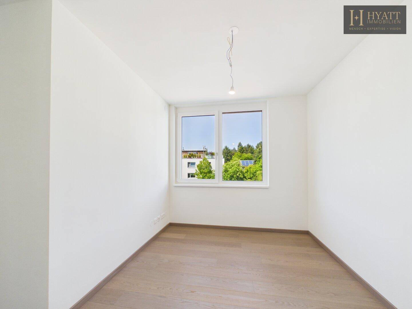 Leeres, helles Schlafzimmer mit großen Fenstern und Holzboden.